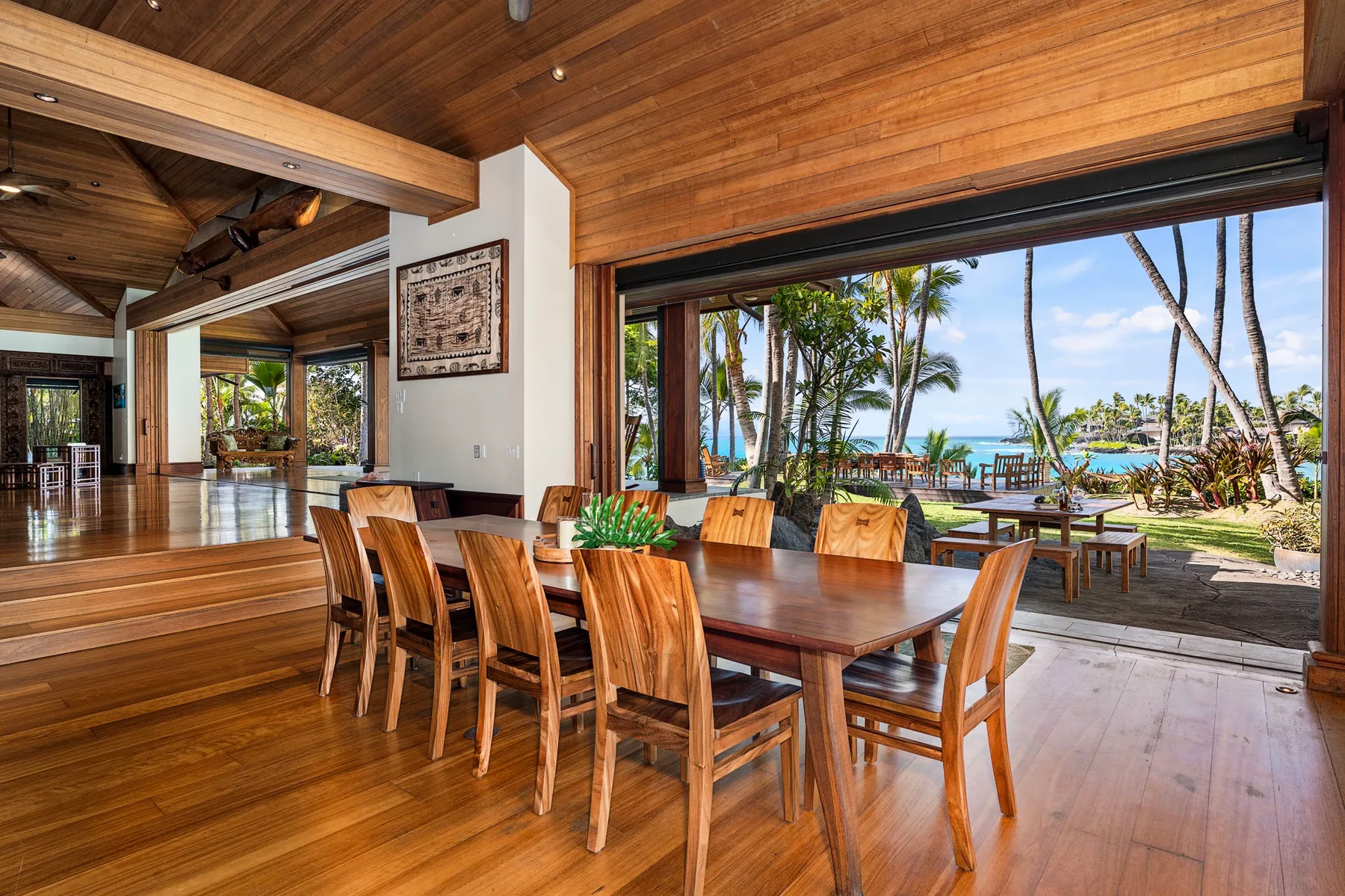 A dining area with wooden tables and seating opens onto a garden and water view.