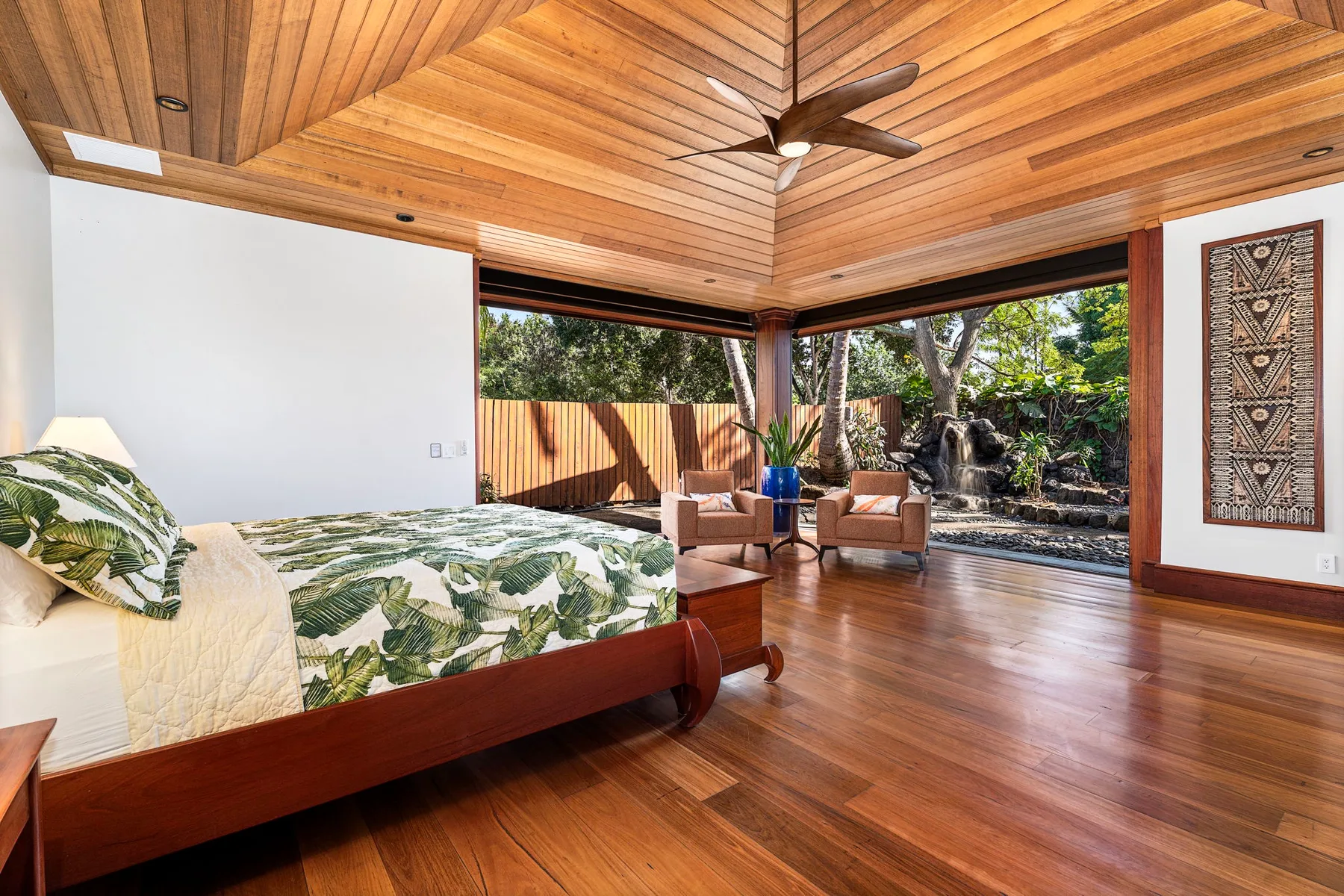 A bedroom with a bed, wooden ceiling, and open views to a garden.