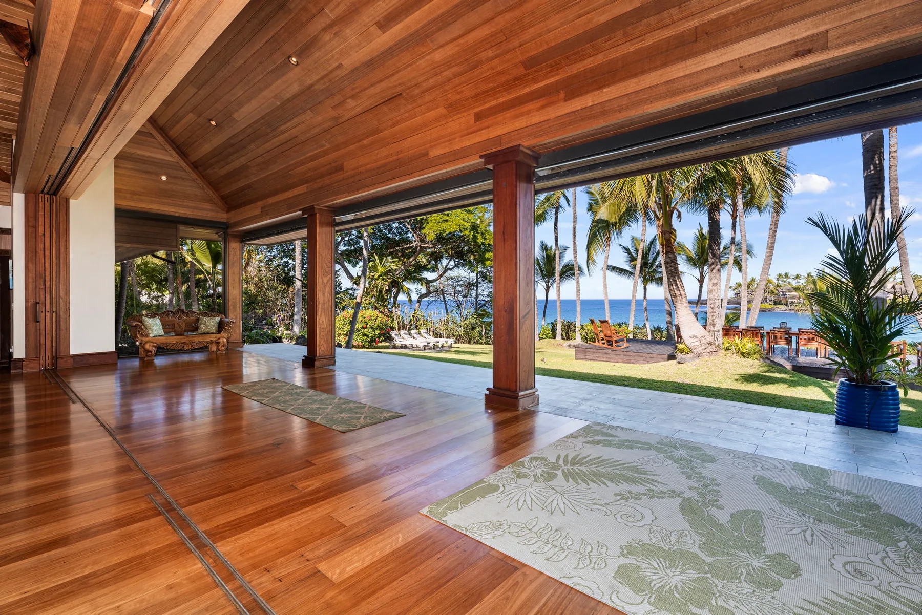 An open-sided wooden pavilion overlooks a tropical garden and the ocean.