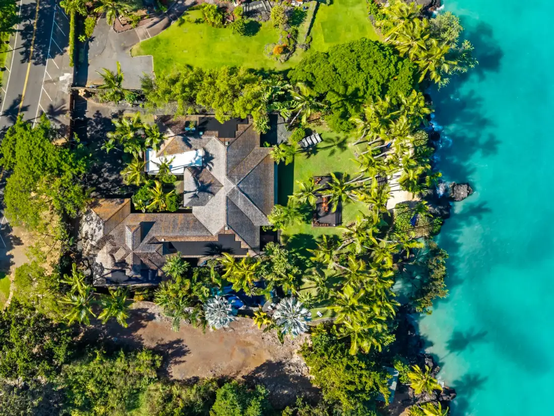 An aerial view of a tropical property beside clear turquoise water.