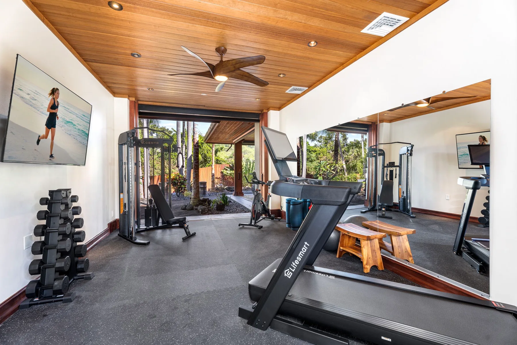 A gym with a treadmill, weight equipment, and large windows overlooking greenery.