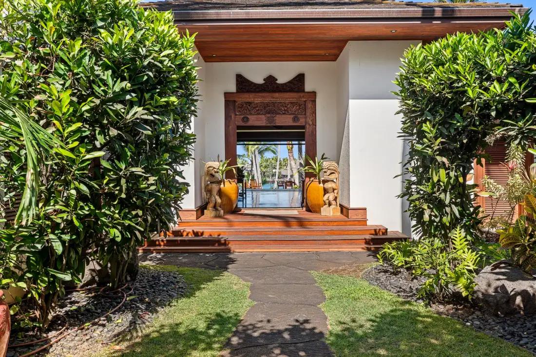 A garden path leads to a carved wooden entrance framed by tropical greenery.