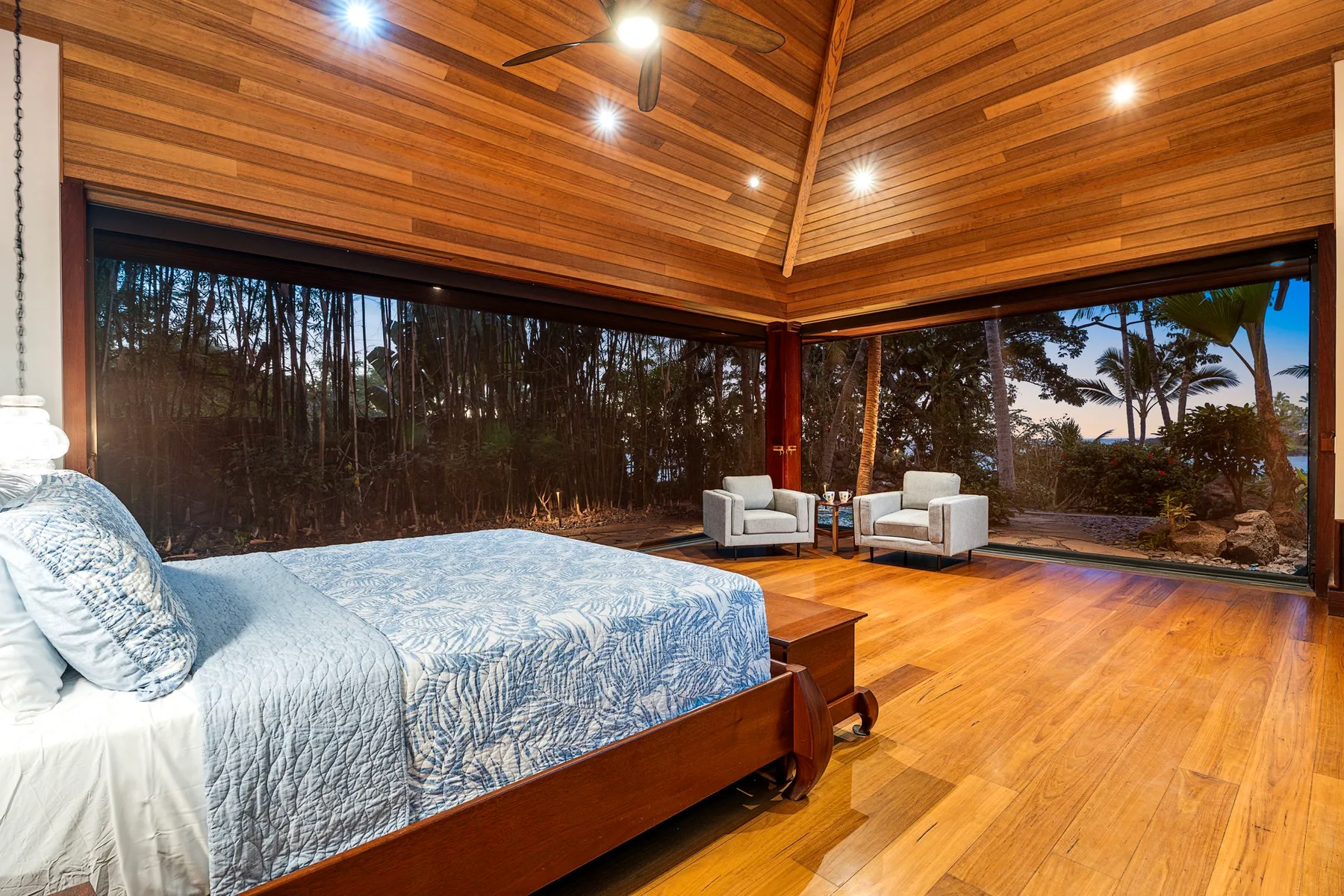 A bedroom with a bed and two armchairs beside large windows.