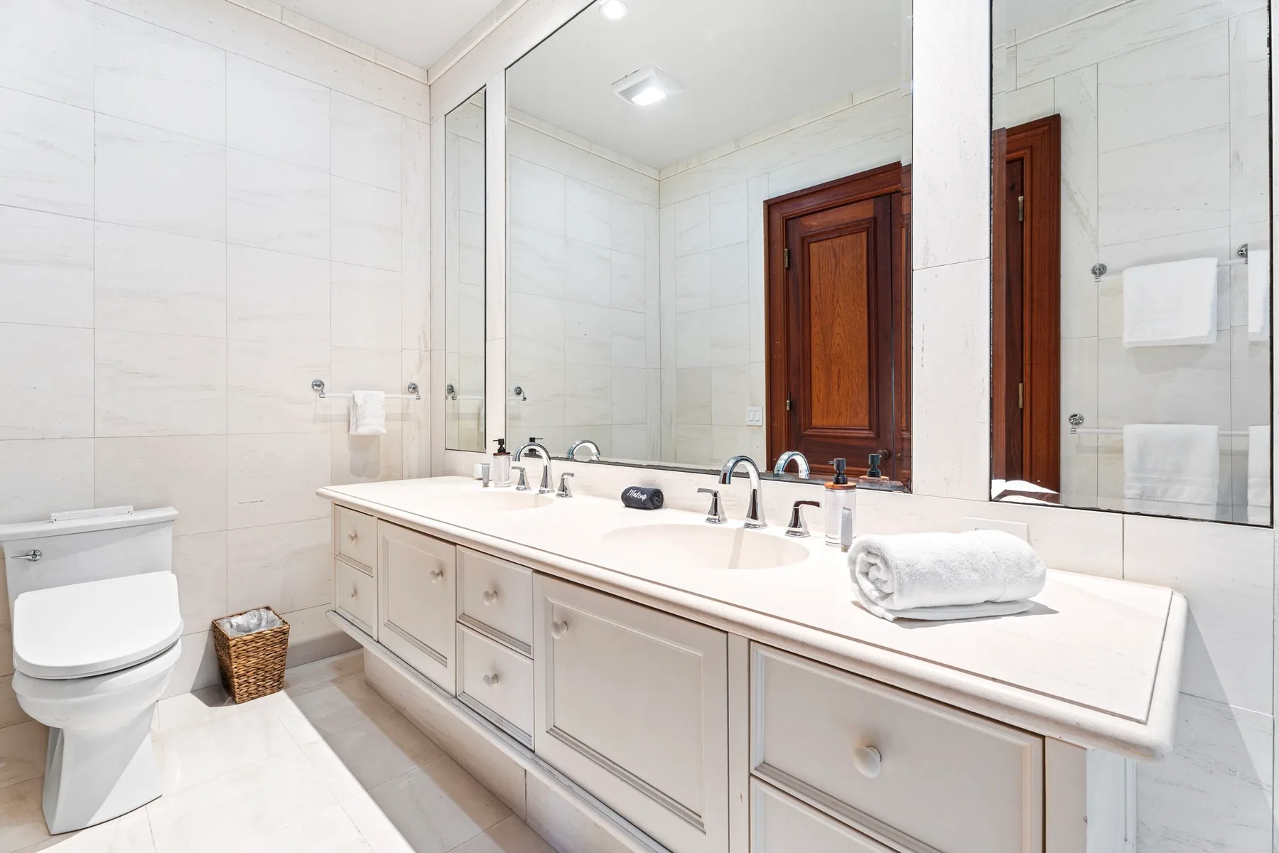 A bright bathroom with a long vanity, mirror, and toilet.