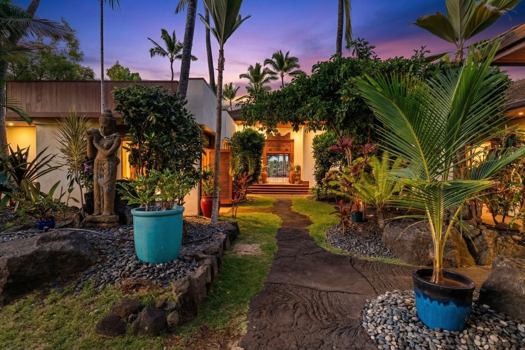 A landscaped garden path leads toward a warmly lit building at dusk.