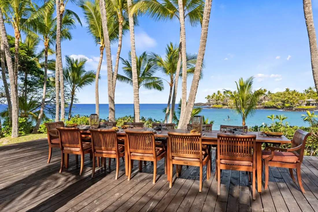 An outdoor dining area with a long wooden table overlooks the ocean.