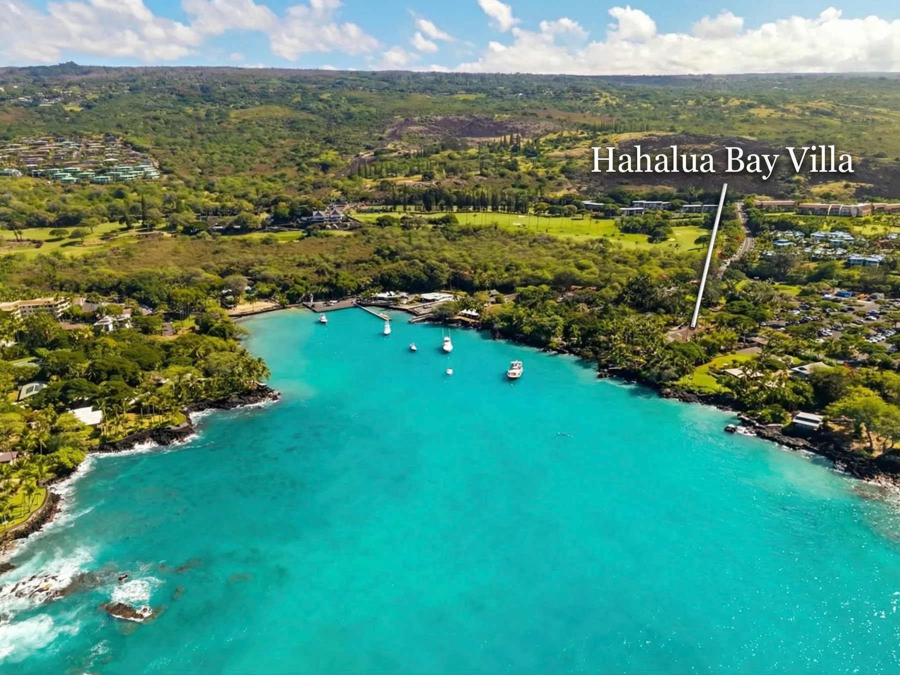 Aerial view of a turquoise bay with boats and green hills along the shore.