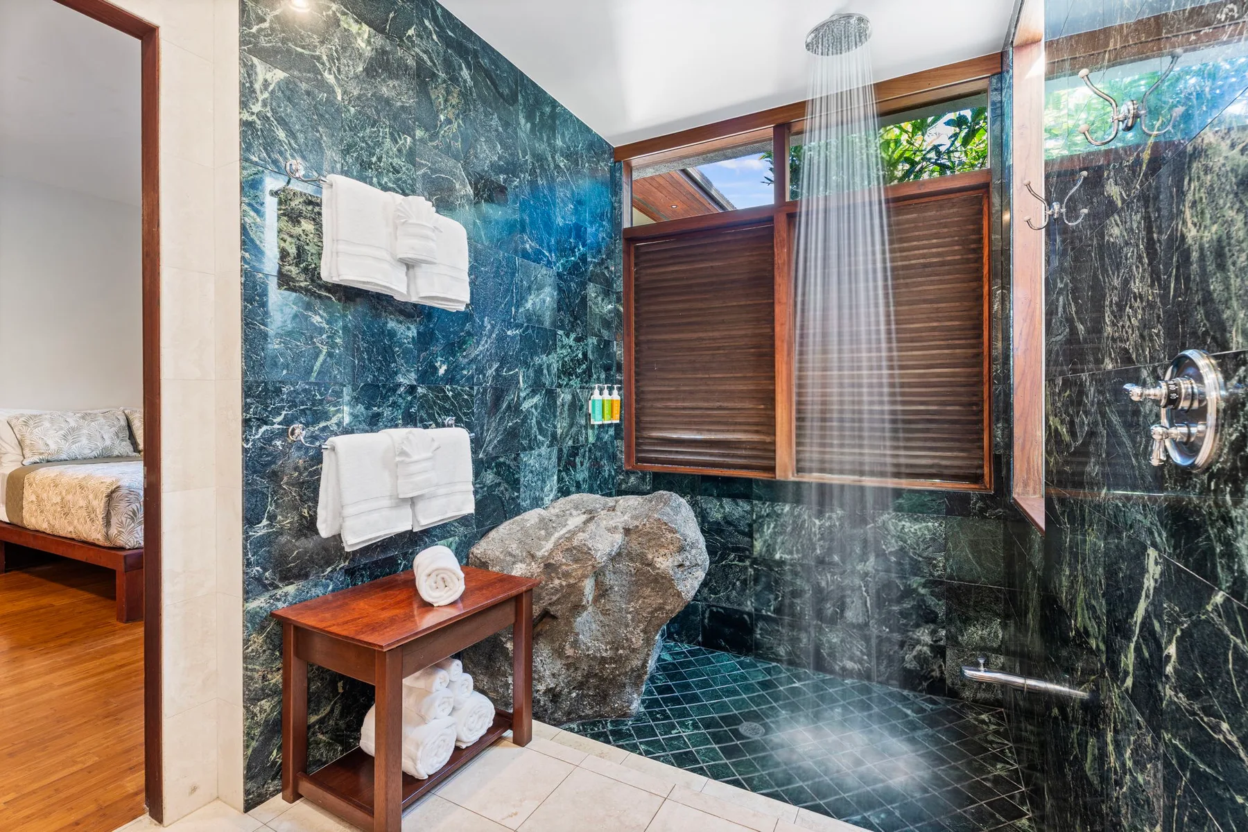 A tiled bathroom with a shower, wooden window shutters, and folded towels.