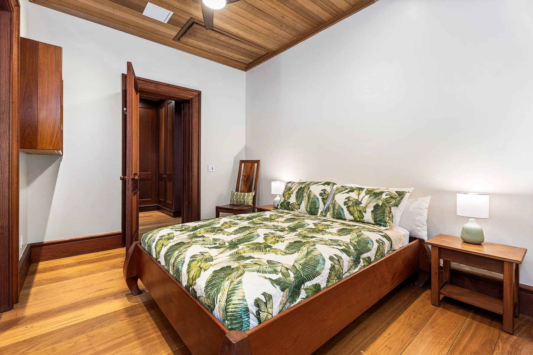 A bedroom with a wooden bed and green leaf-patterned bedding.