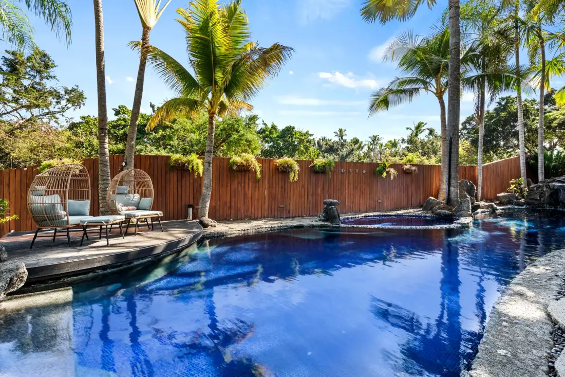 An outdoor swimming pool beside a wooden fence and palm trees.