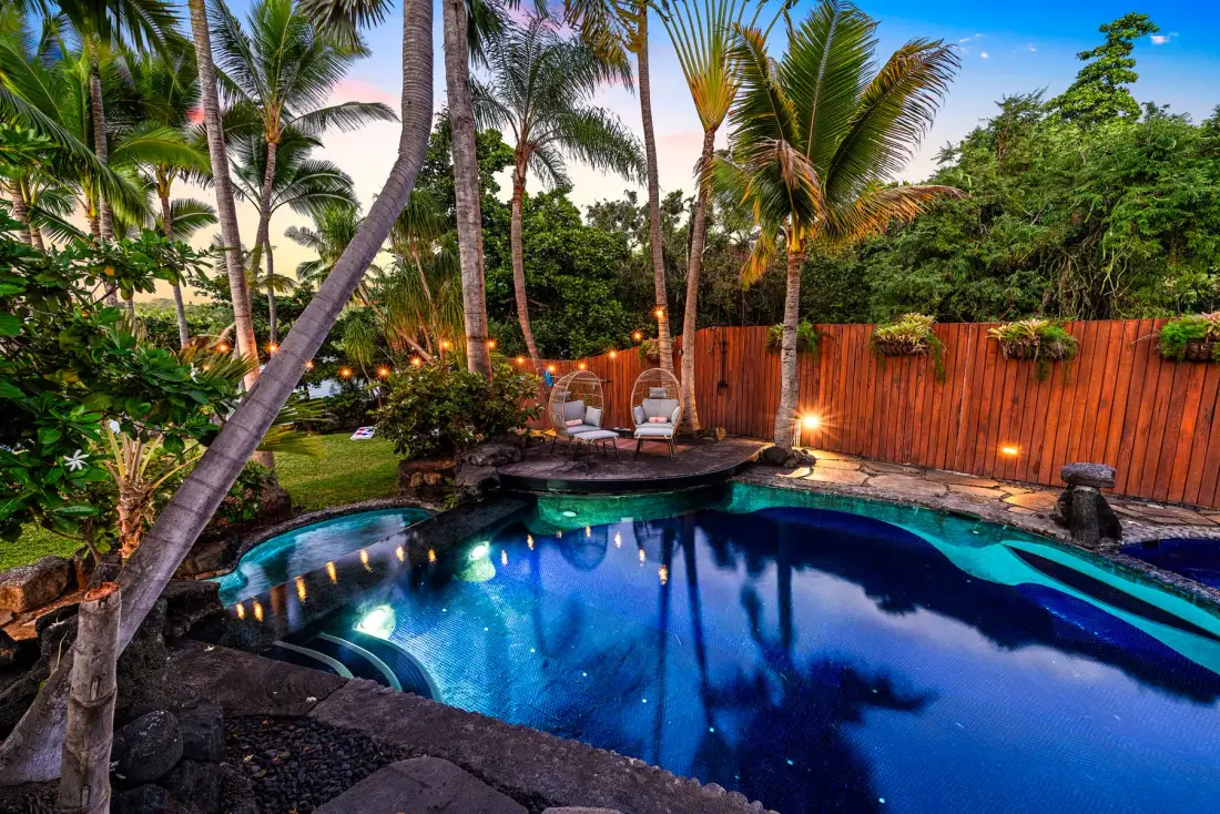 A swimming pool sits among palm trees and lush tropical greenery.