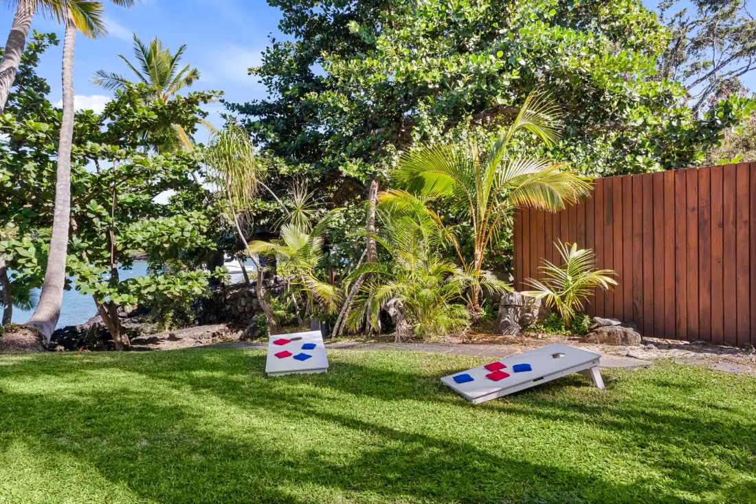 A grassy outdoor recreation area with cornhole boards and tropical plants.