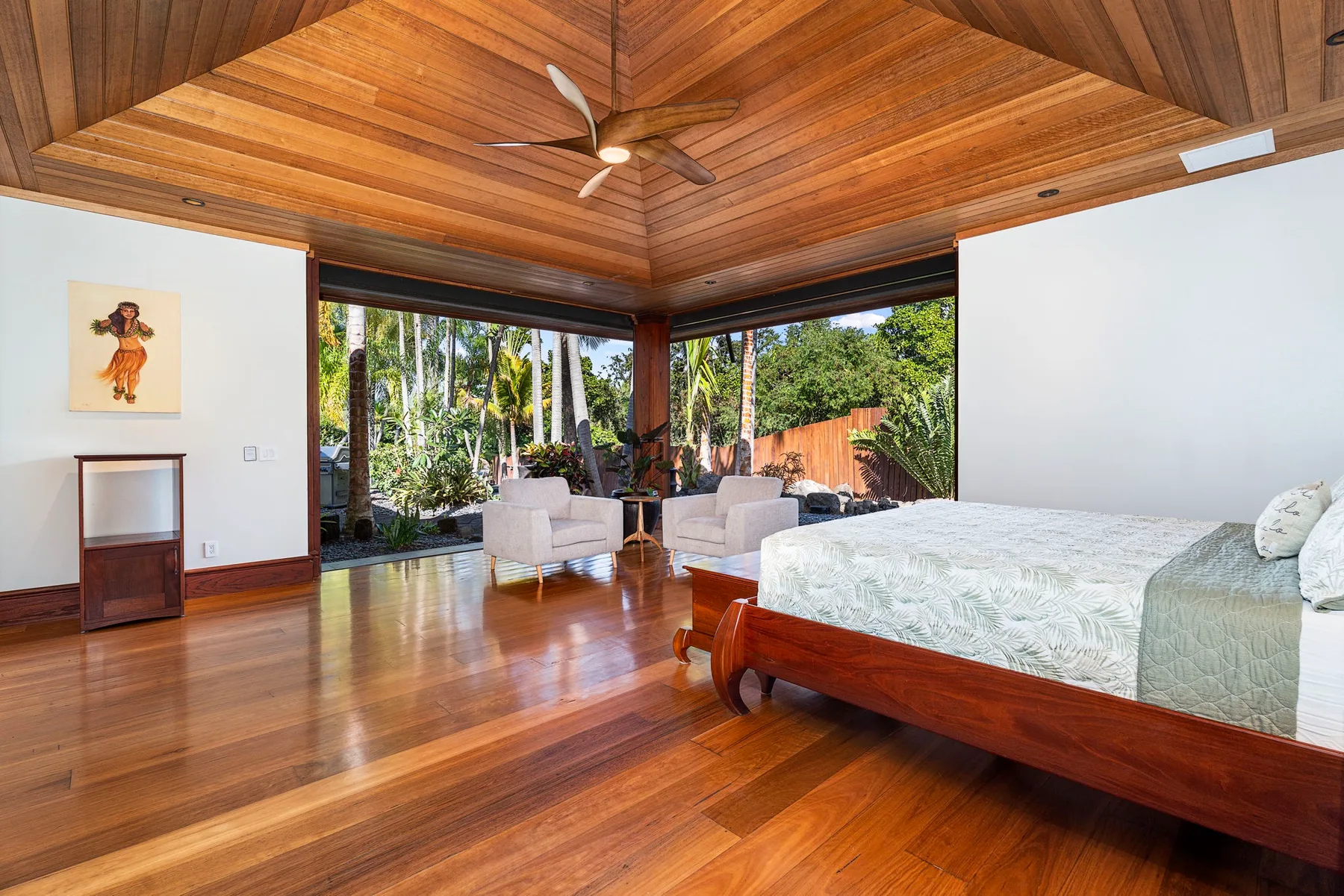 A bedroom with a wooden bed, seating, and large windows overlooking greenery.