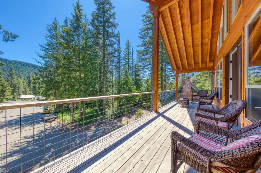 A covered wooden deck with woven seating overlooks a tree-lined road.