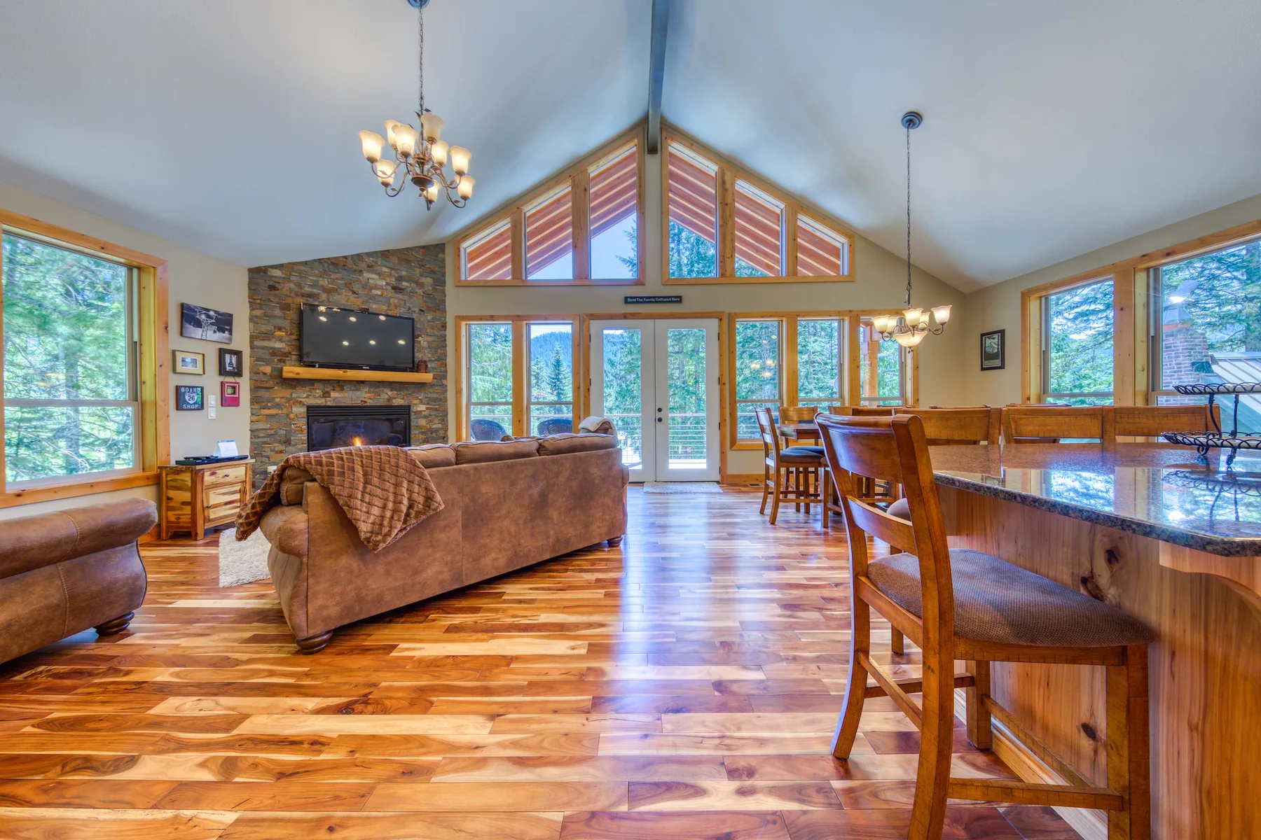 A vaulted living and dining room with large windows and a stone fireplace.