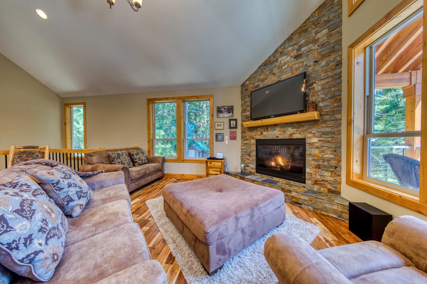 A living room with a stone fireplace, television, and central ottoman.