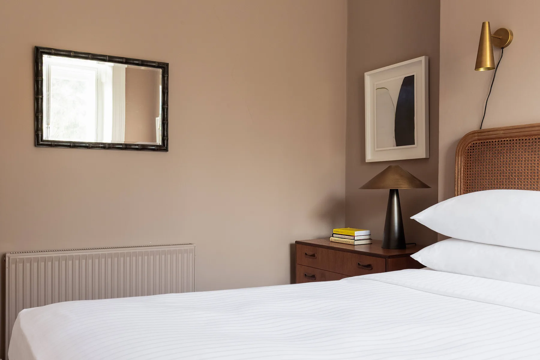 A bedroom with a neatly made bed, a bedside table, and a wall mirror.