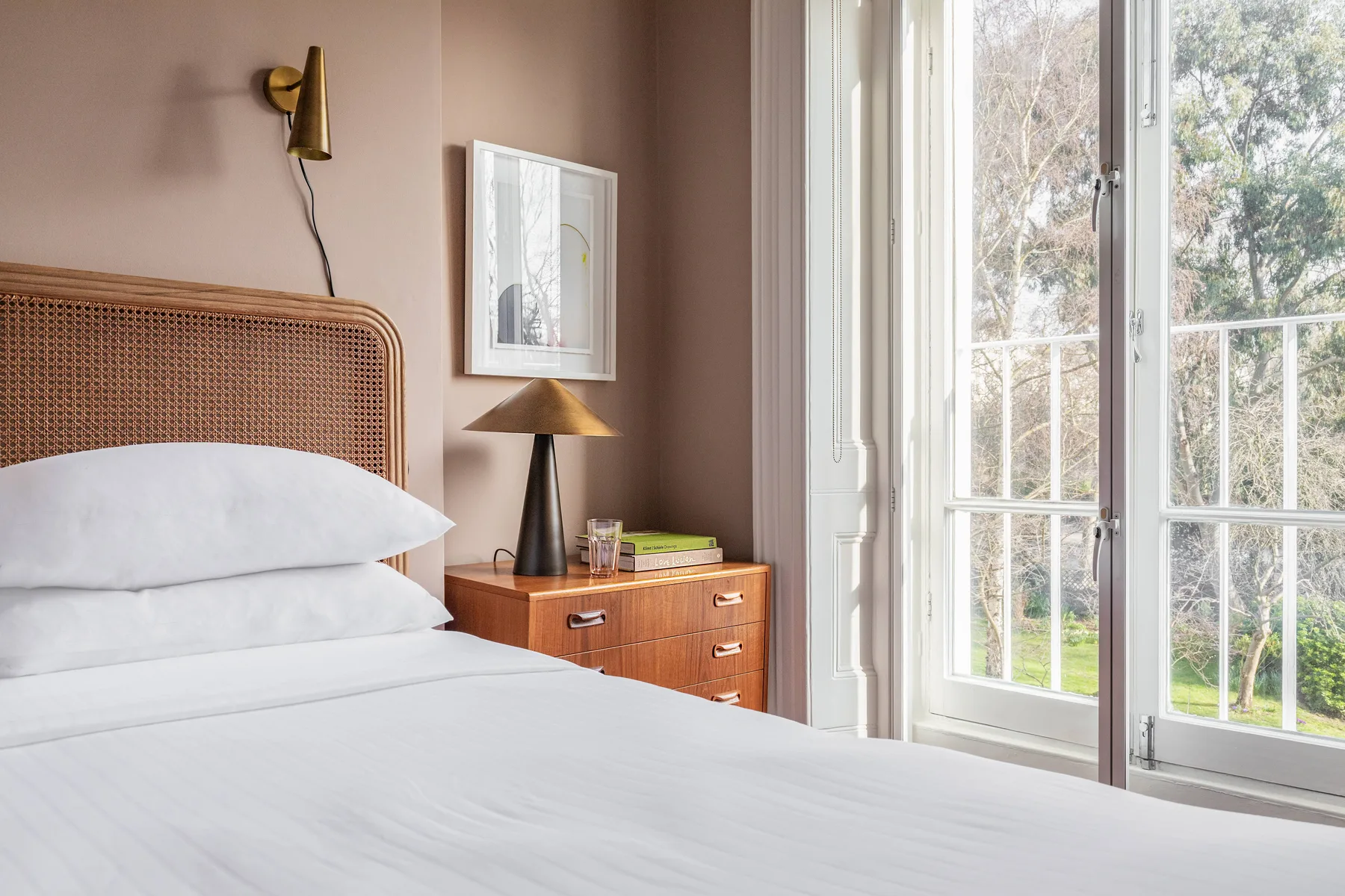 A bright bedroom with a neatly made bed beside tall glass doors.