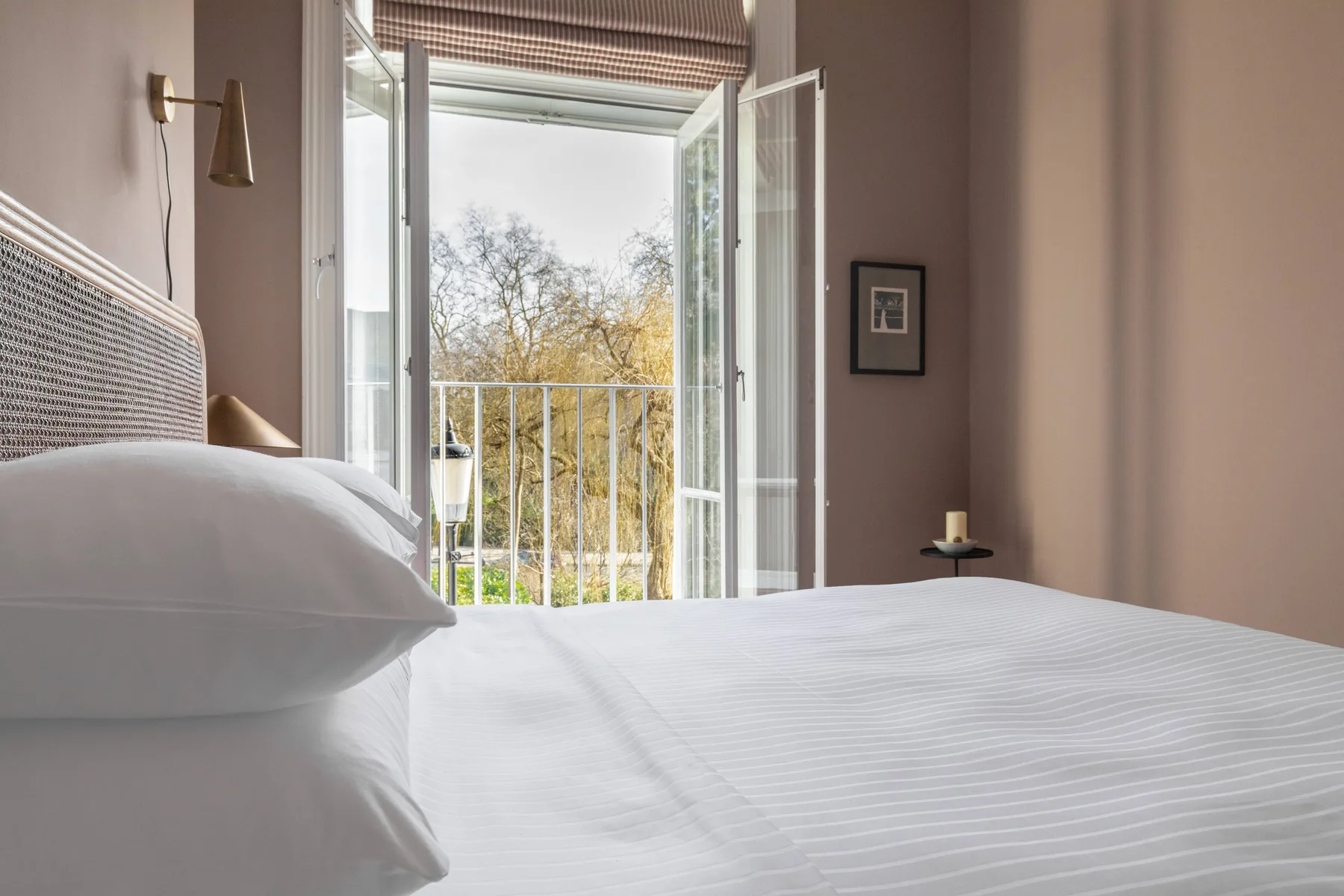 A bedroom with white bedding and open glass doors overlooking trees.