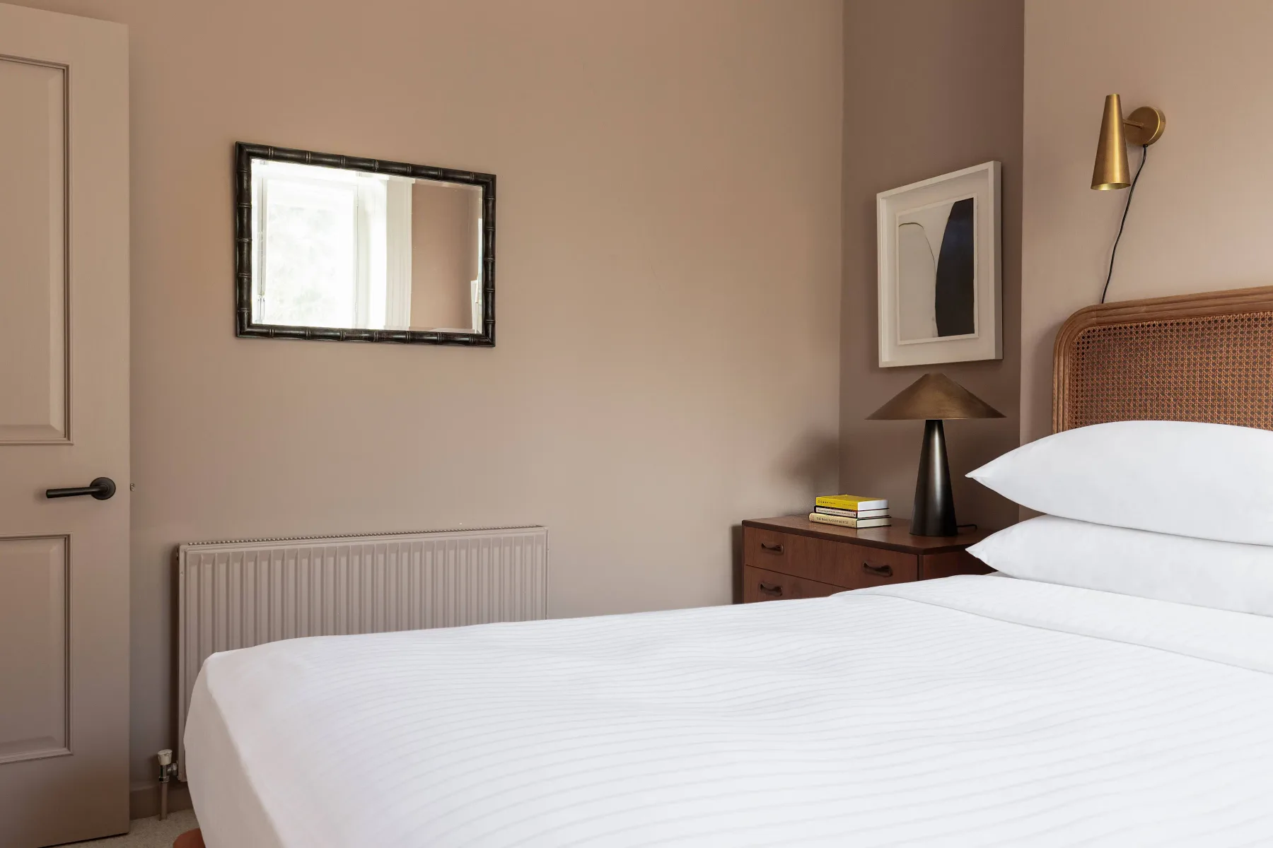 A bedroom with a neatly made bed, bedside table, and wall mirror.