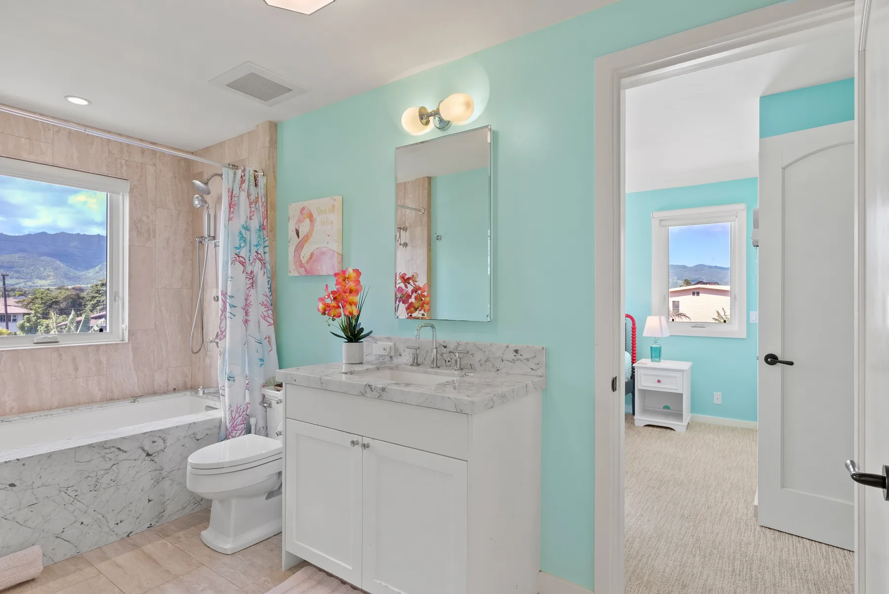 Un baño con tocador, lavabo y ducha junto a la entrada de un dormitorio.