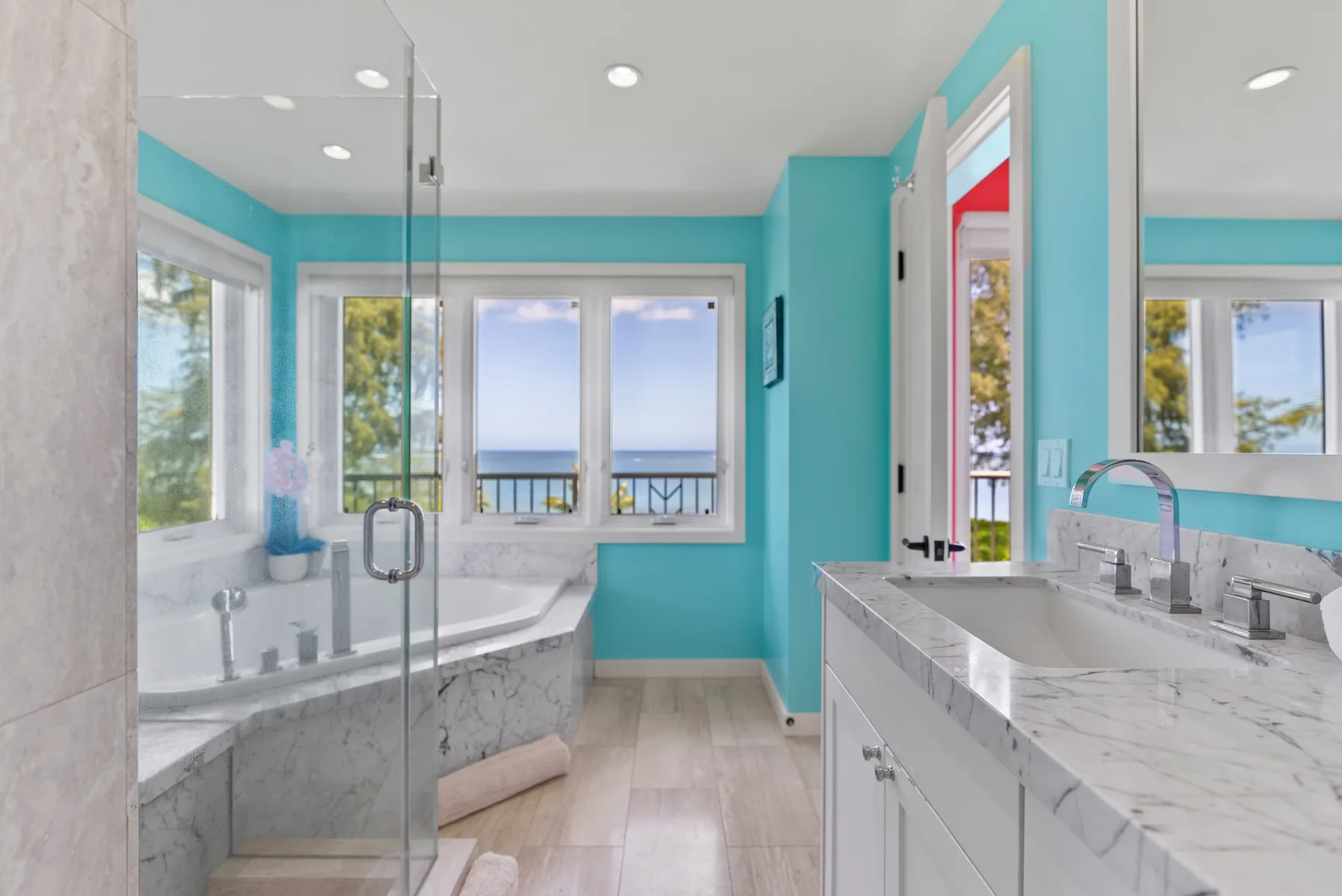 Un baño luminoso con bañera, ducha de vidrio y ventanas con vistas al agua.