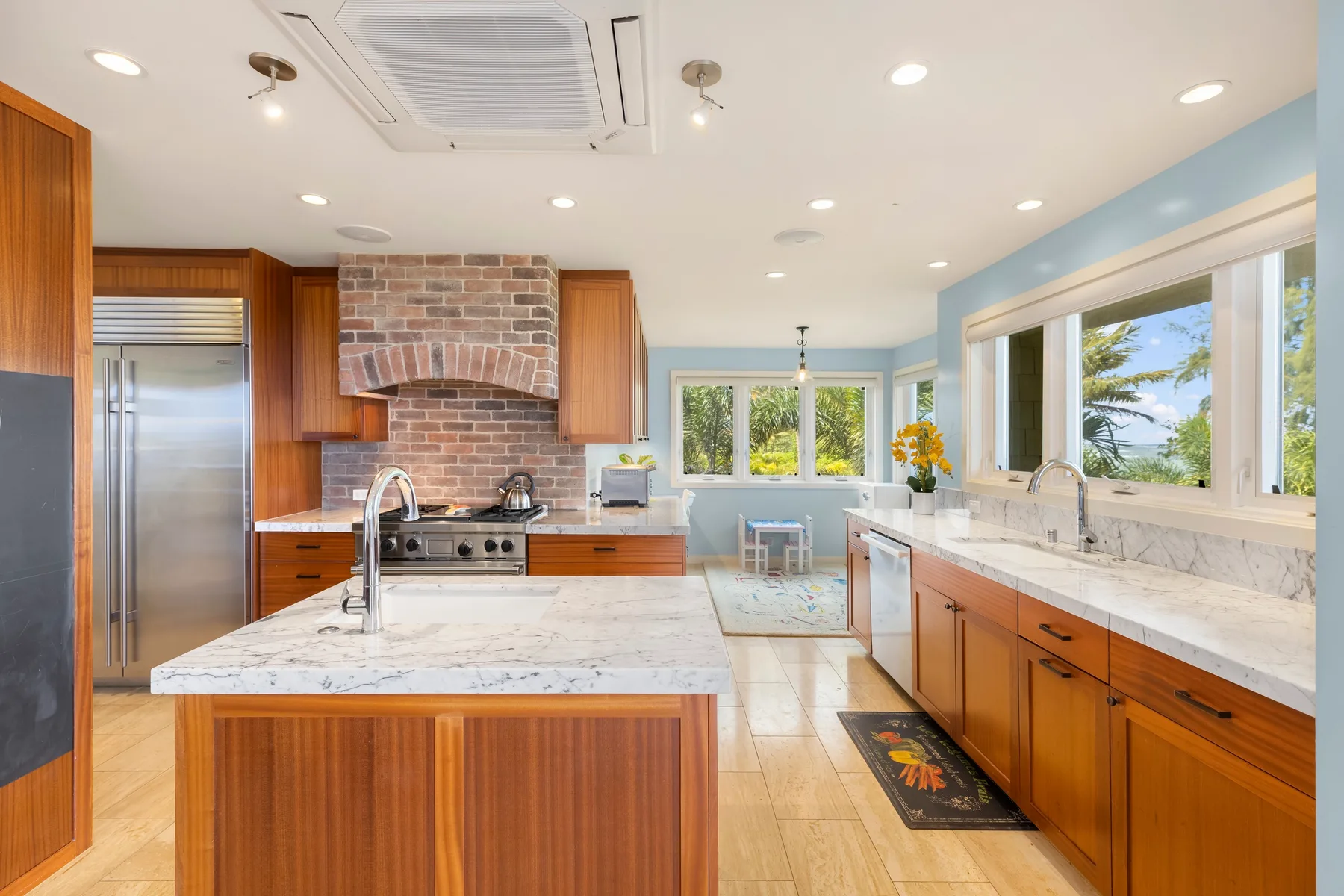Una cocina luminosa con gabinetes de madera, encimeras de piedra y grandes ventanas.