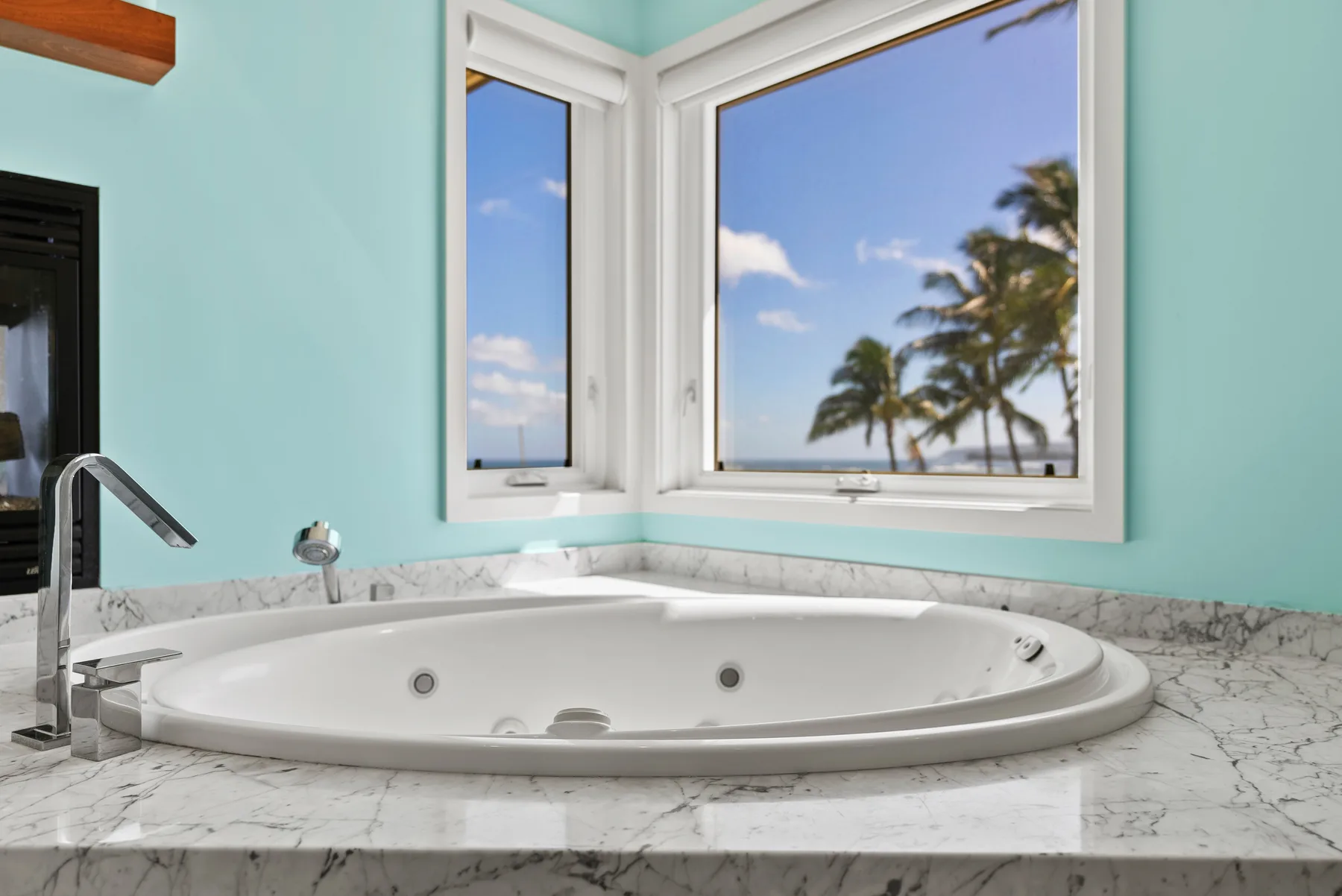 Una bañera empotrada está bajo ventanas con vistas a palmeras y al cielo azul.