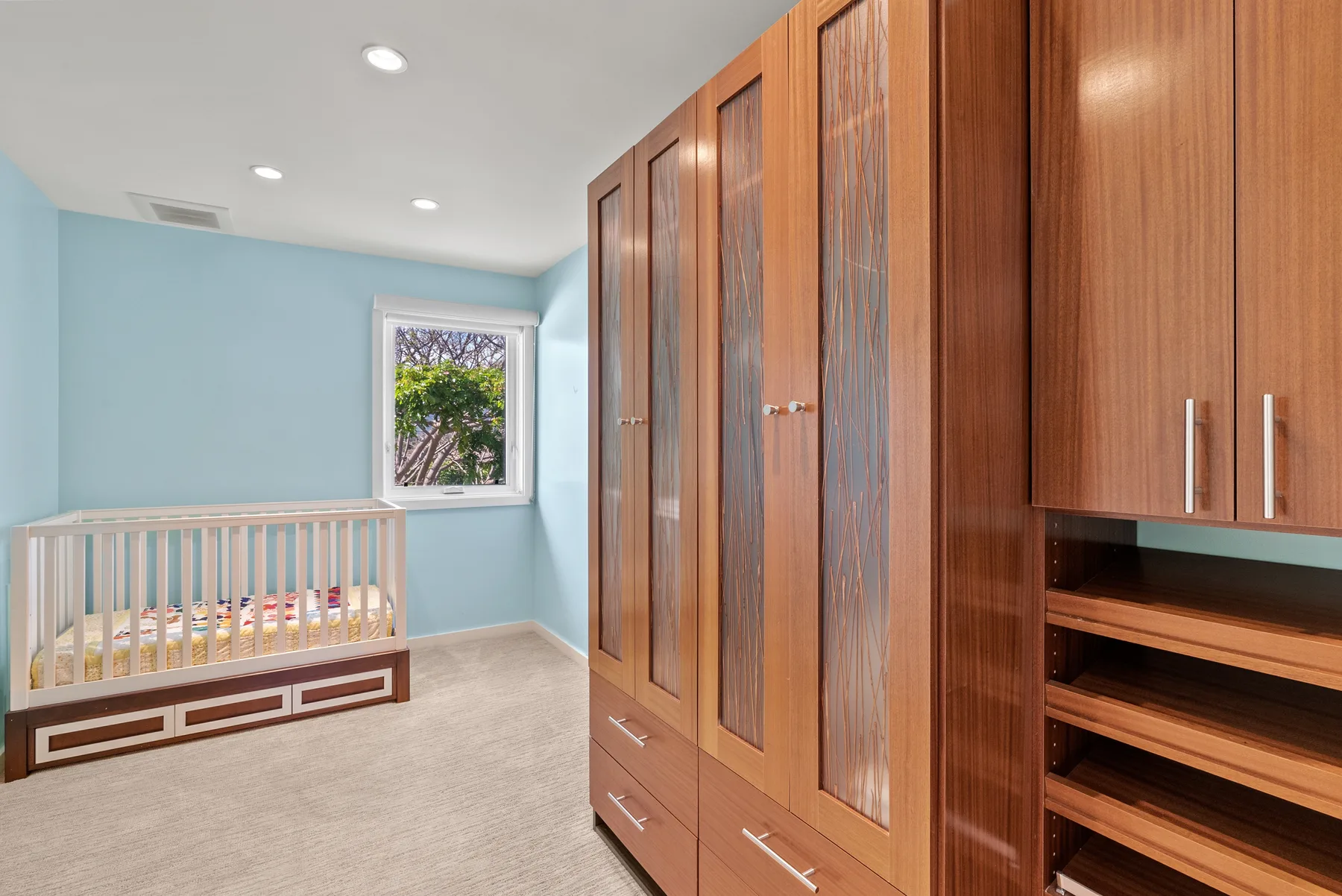 Un cuarto infantil con una cuna de madera junto a armarios empotrados y estantes abiertos.
