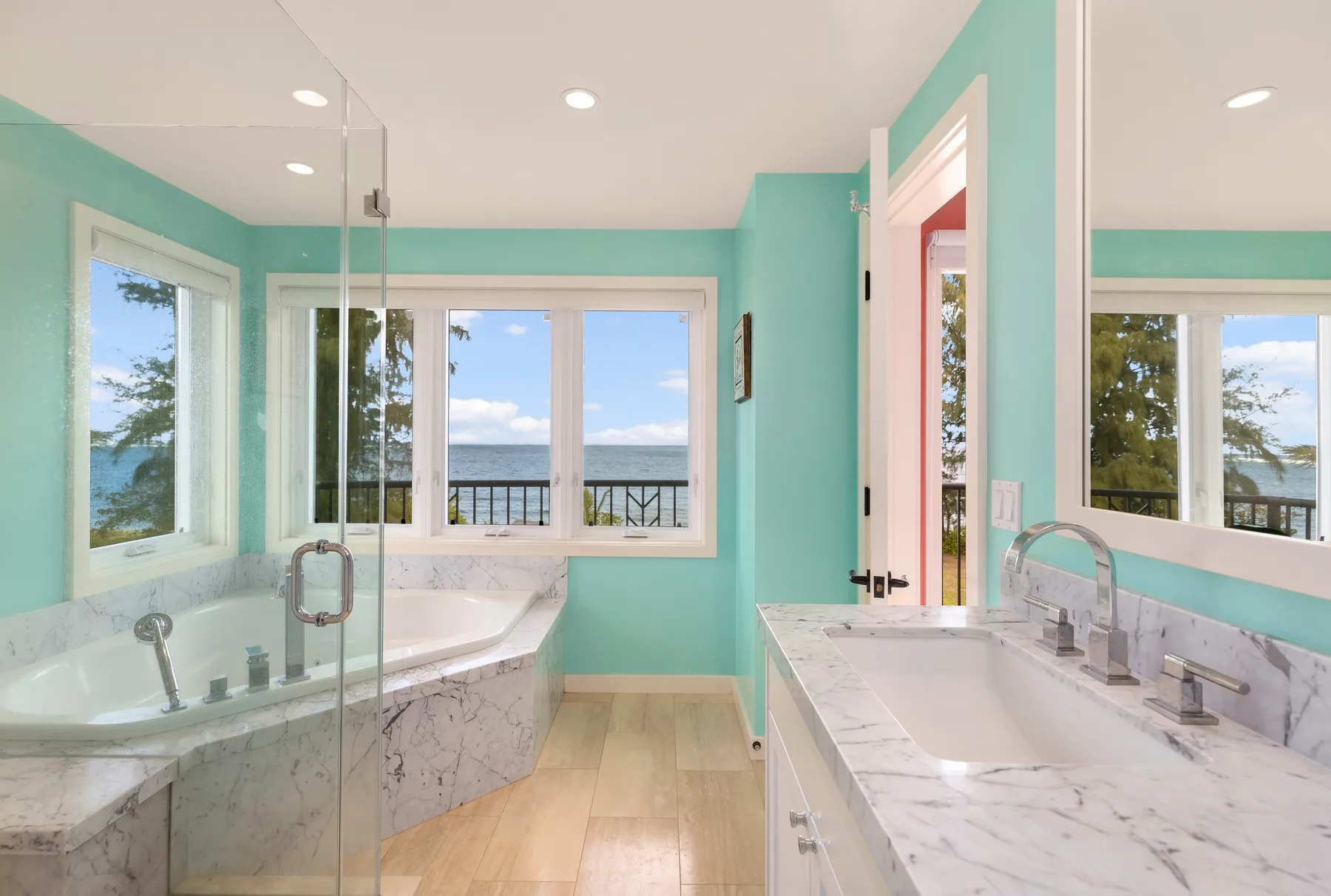 Un baño luminoso tiene una bañera y un lavabo junto a ventanas con vista al agua.