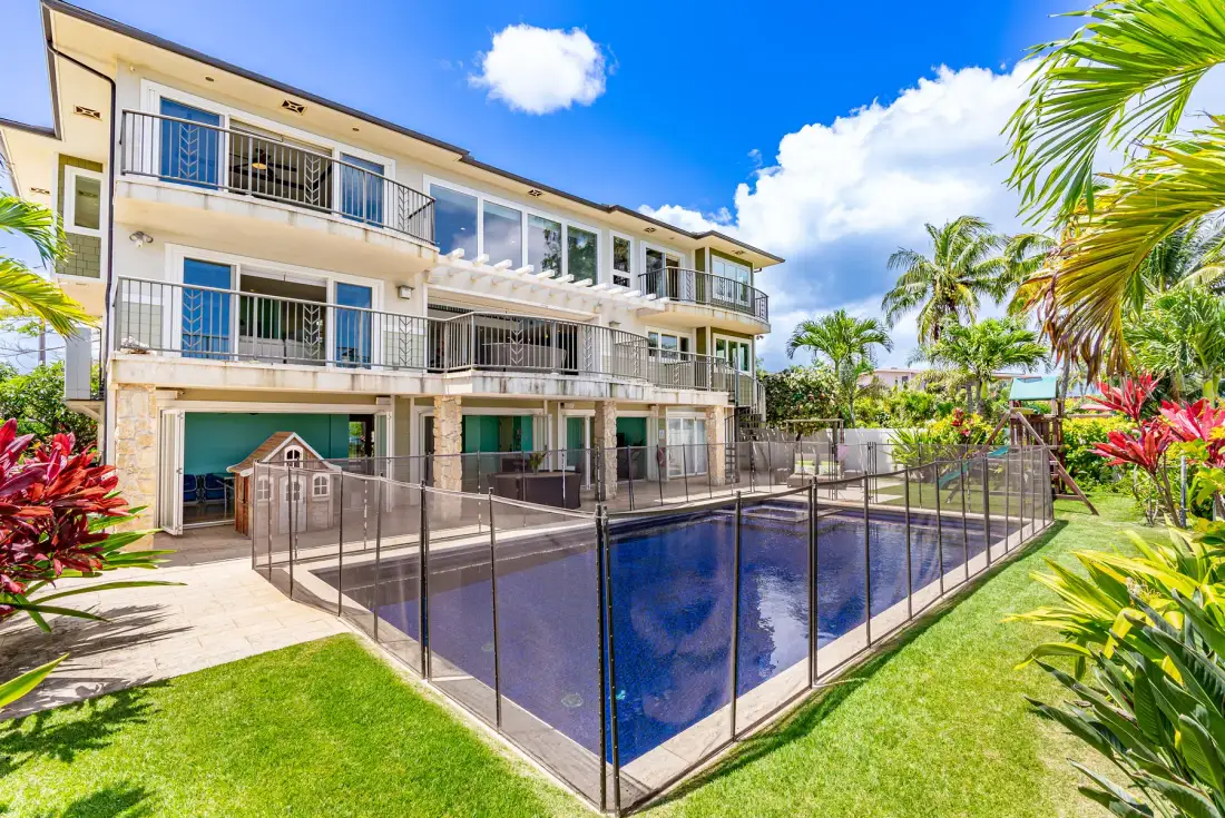Un edificio de apartamentos da a una piscina cercada, rodeada de vegetación tropical.