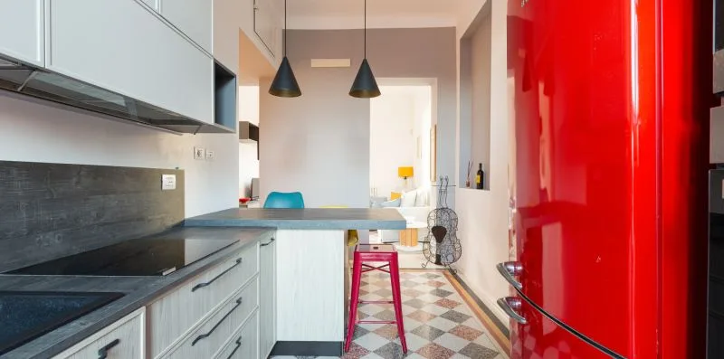 A modern kitchen with light cabinetry, dark counters, and a red refrigerator.