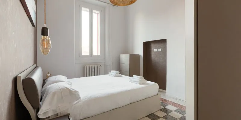 A bright bedroom with a neatly made bed and a tall window.
