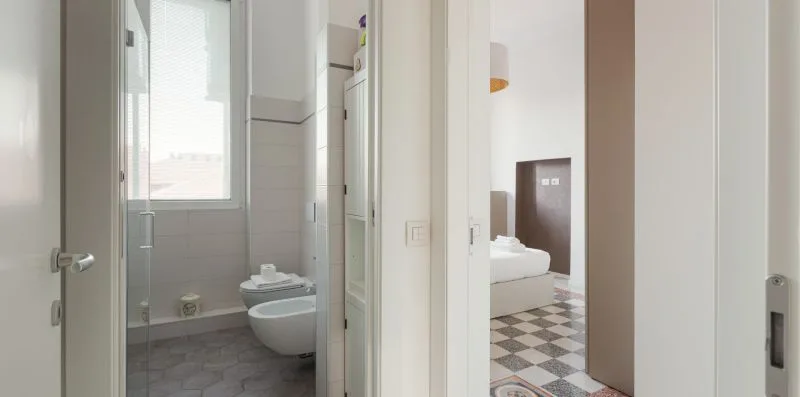 A tiled bathroom with a toilet and sink, viewed through an open doorway.