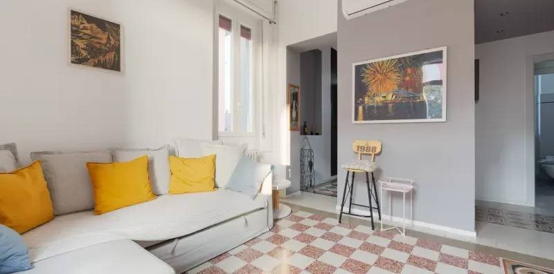 A bright living room with seating, colorful wall art, and a patterned tile floor.