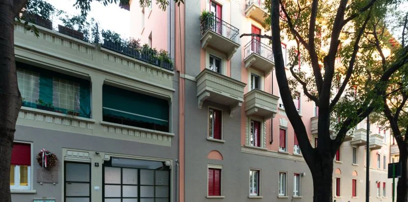 Street view of apartment buildings with balconies and trees along the sidewalk.