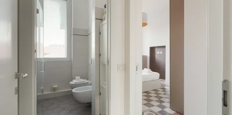 A bathroom with a toilet and sink opens onto a bedroom with a bed.