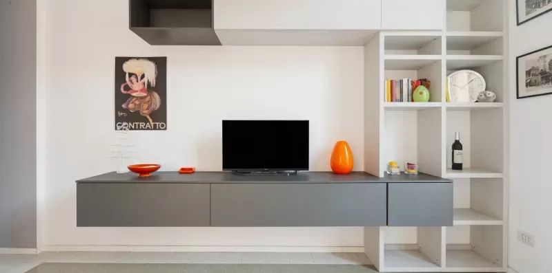 A modern living room wall has a television above a floating cabinet and open shelving.