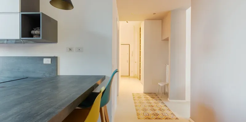 A modern kitchen opens onto a bright hallway with patterned floor tiles.