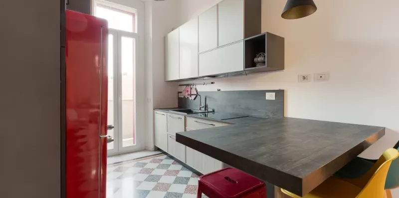A modern kitchen with white cabinets, a dark countertop, and a red refrigerator.