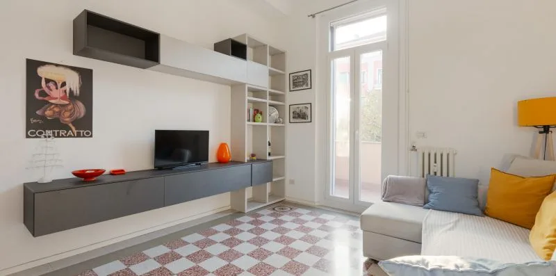 A bright living room with wall-mounted shelving, a television, and seating beside tall glass doors.