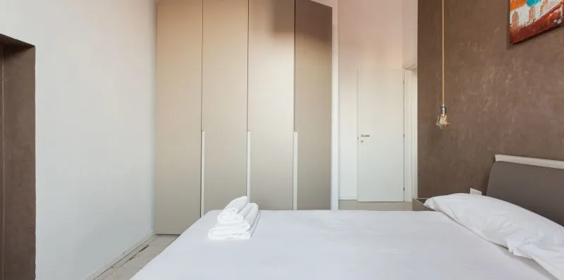 A bedroom with a bed, folded towels, and a wardrobe.