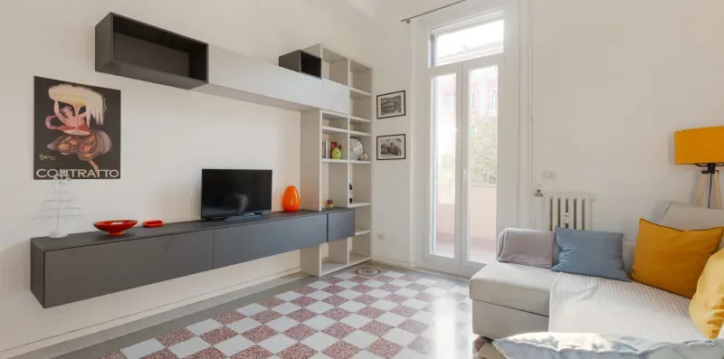A bright living room with a wall-mounted television and seating beside tall windows.