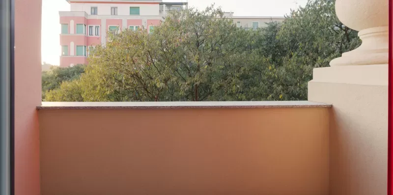 A balcony with a peach-colored wall overlooks leafy trees and nearby buildings.