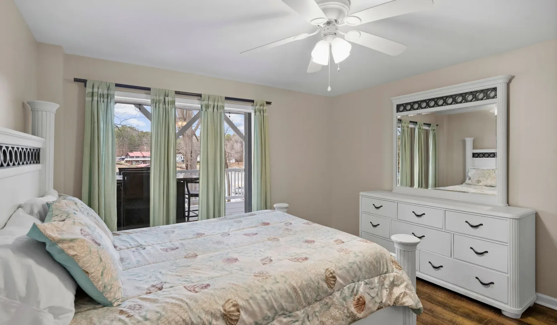 A bedroom with a bed, dresser, and glass doors opening to a balcony.