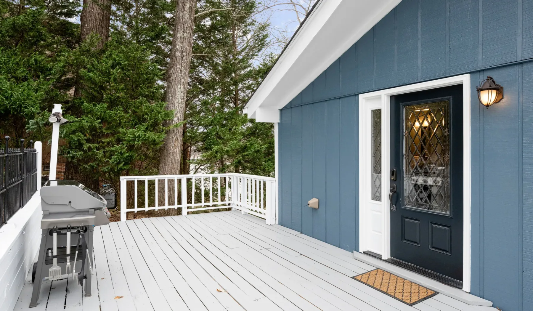 A raised outdoor deck with a grill beside a blue entrance.