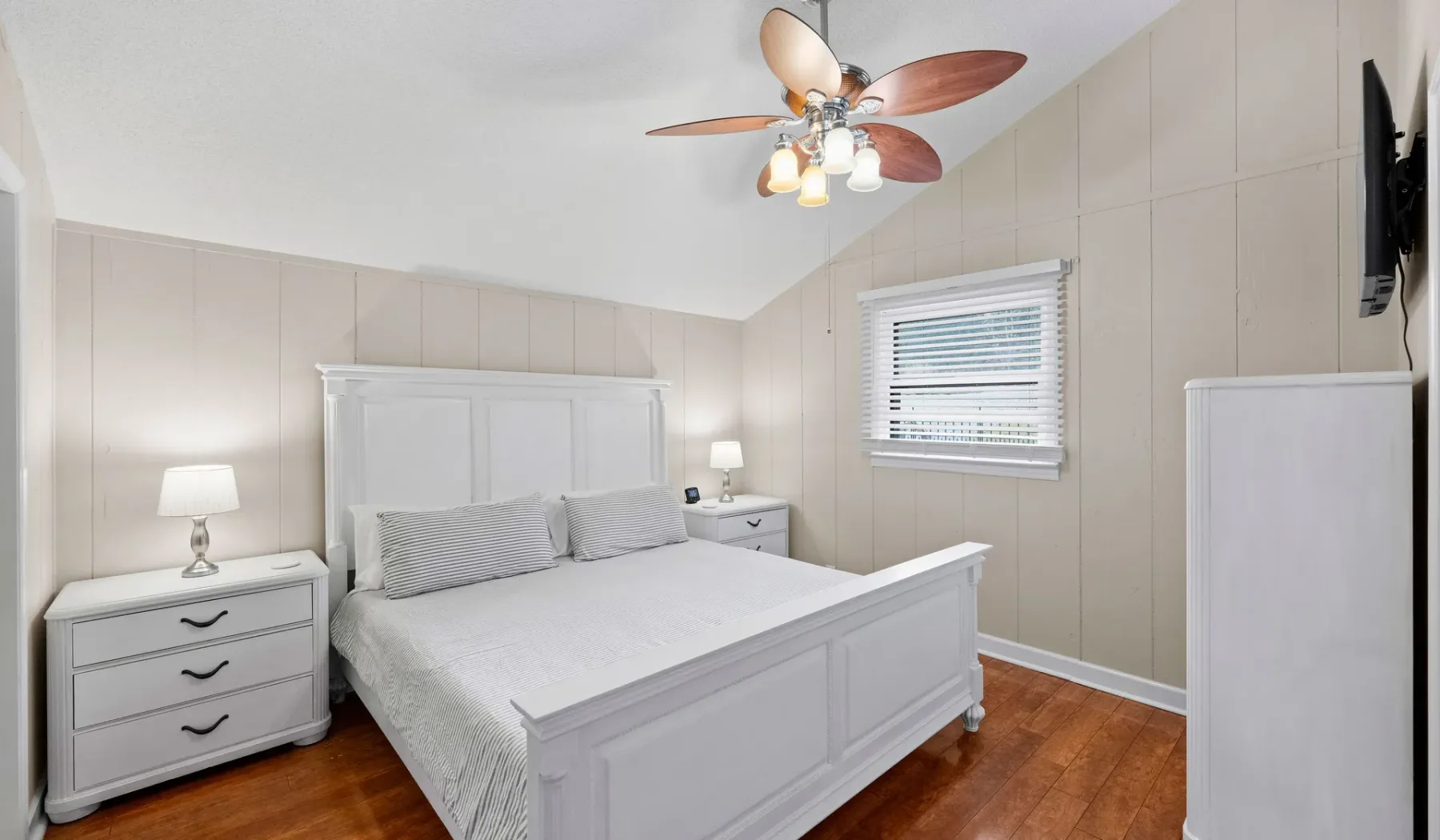 Un dormitorio luminoso con una cama blanca y muebles auxiliares a juego.