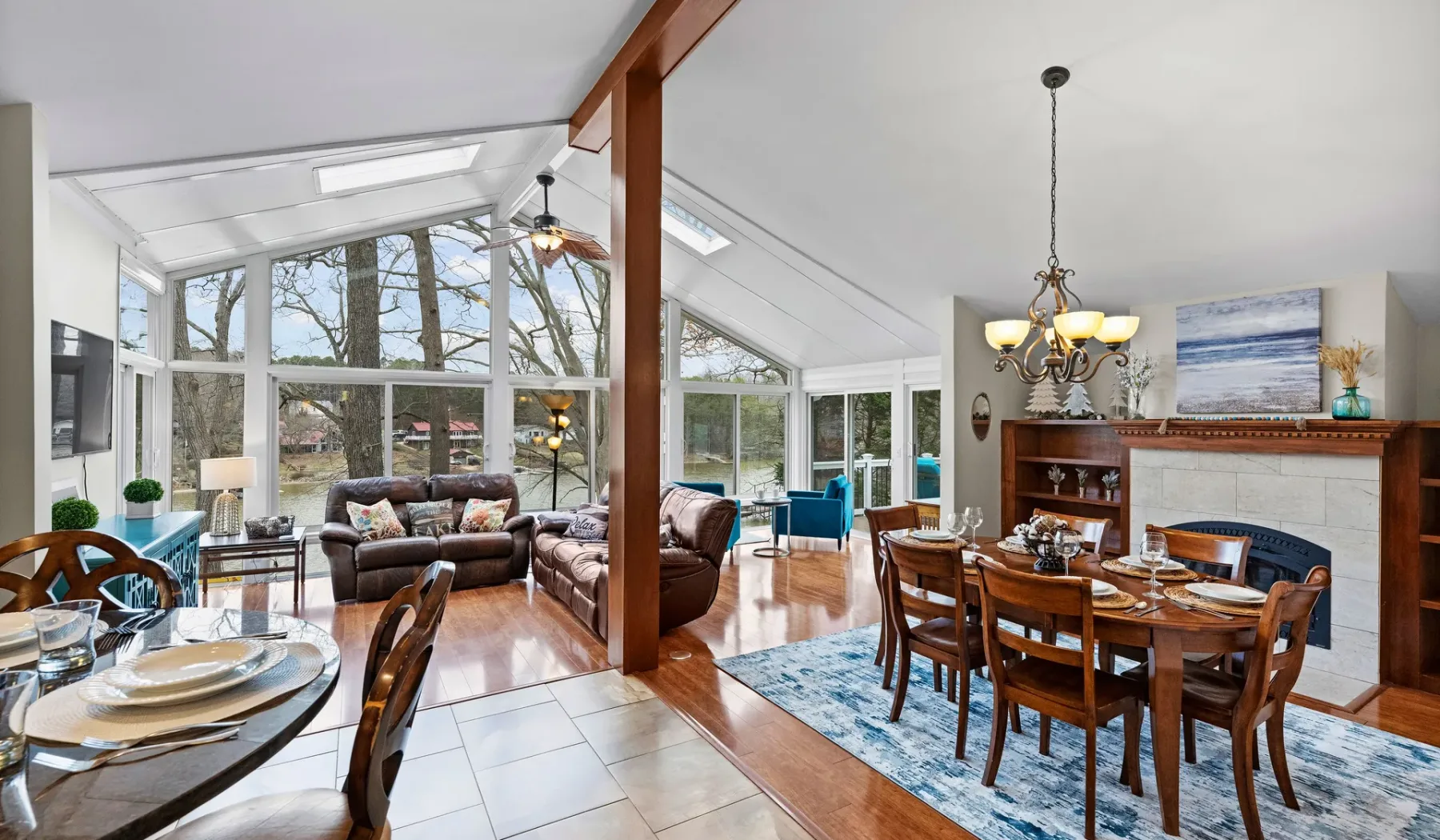 A bright open-plan living and dining room has large windows and a wooden dining table.