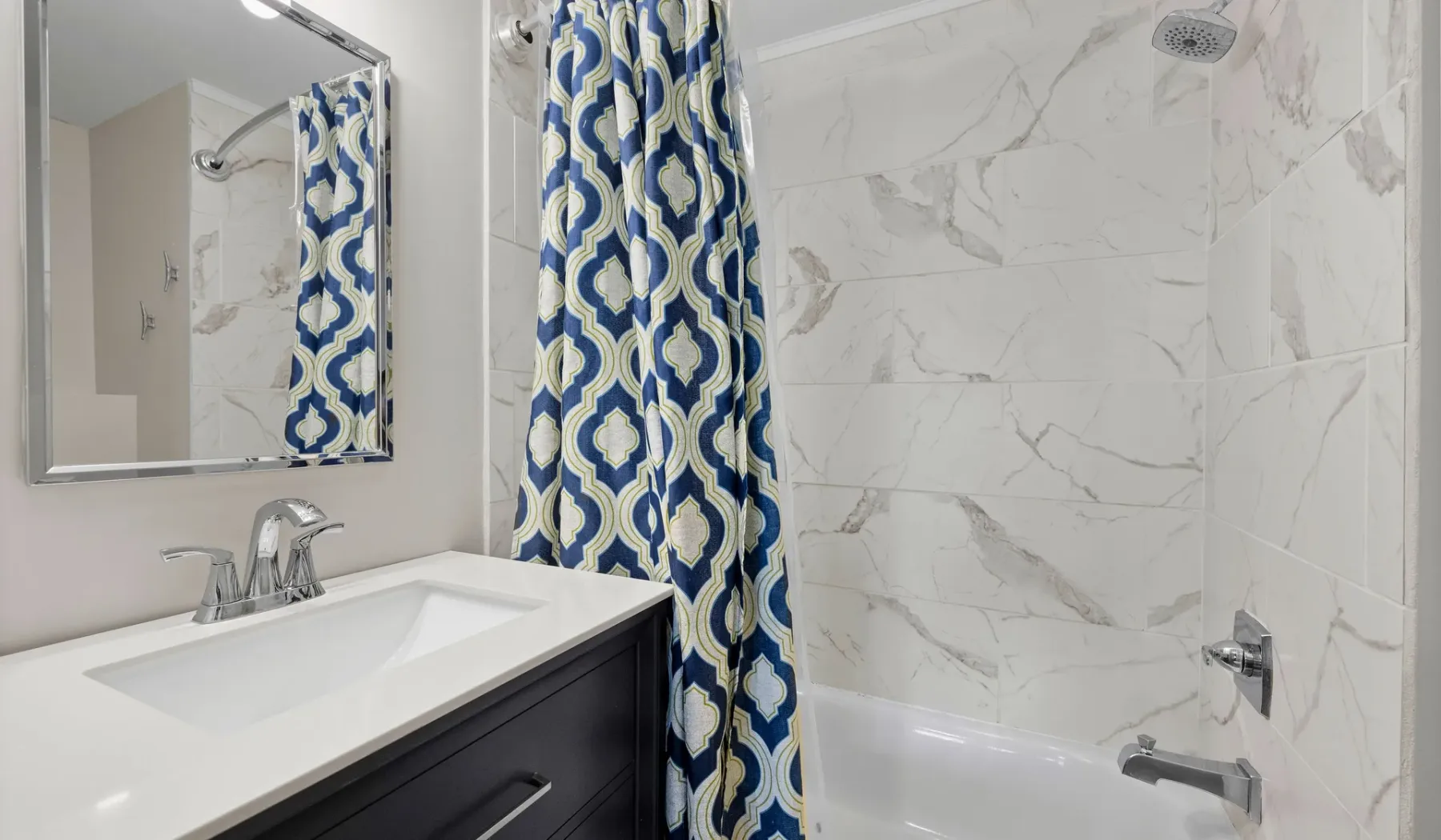 A bathroom with a sink, mirror, and bathtub behind a patterned shower curtain.