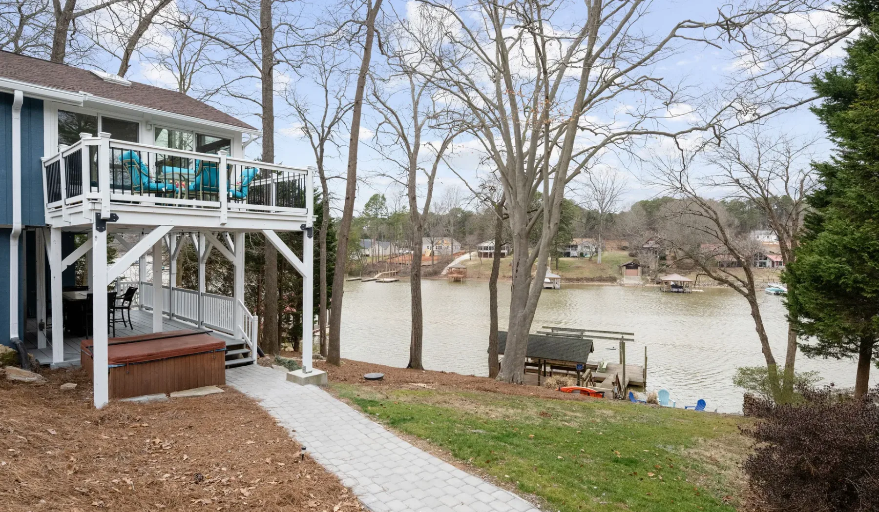 A lakeside house has an elevated deck overlooking the water and a paved path.